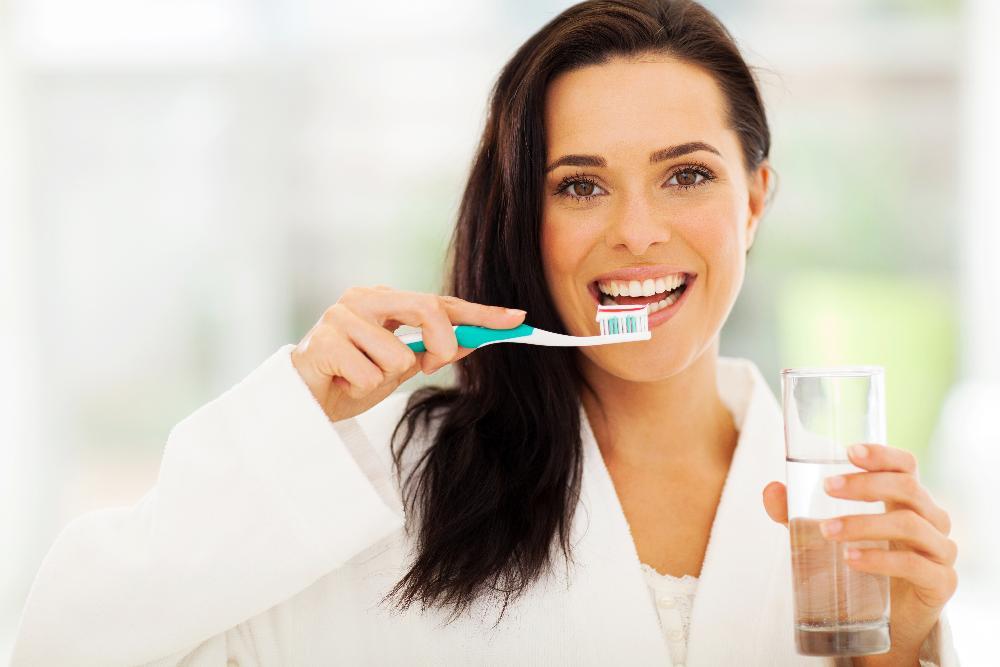 woman brushing her teeth and holding a glass of water